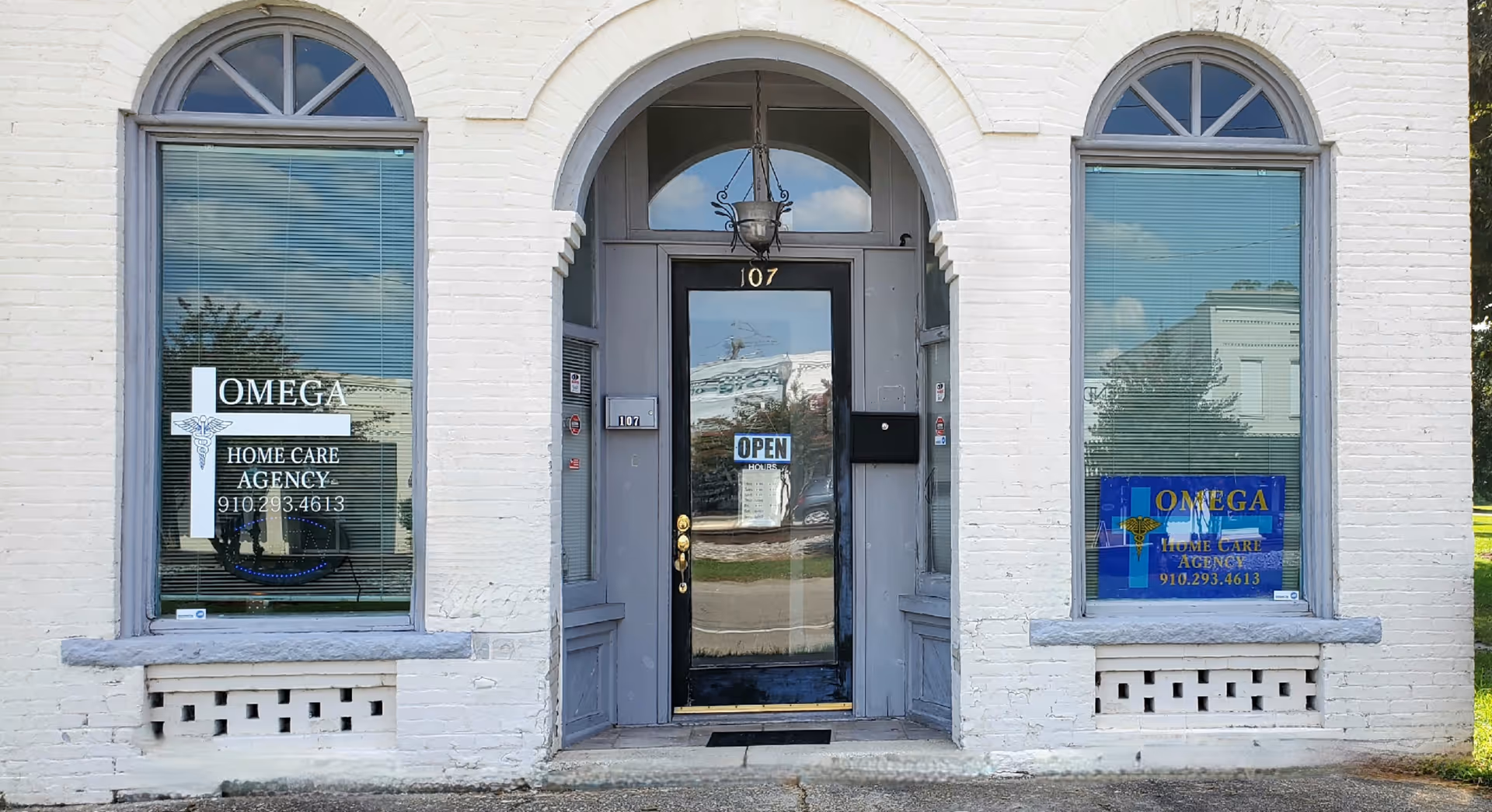 White brick building facade with arched windows and central door for Omega Home Care Agency