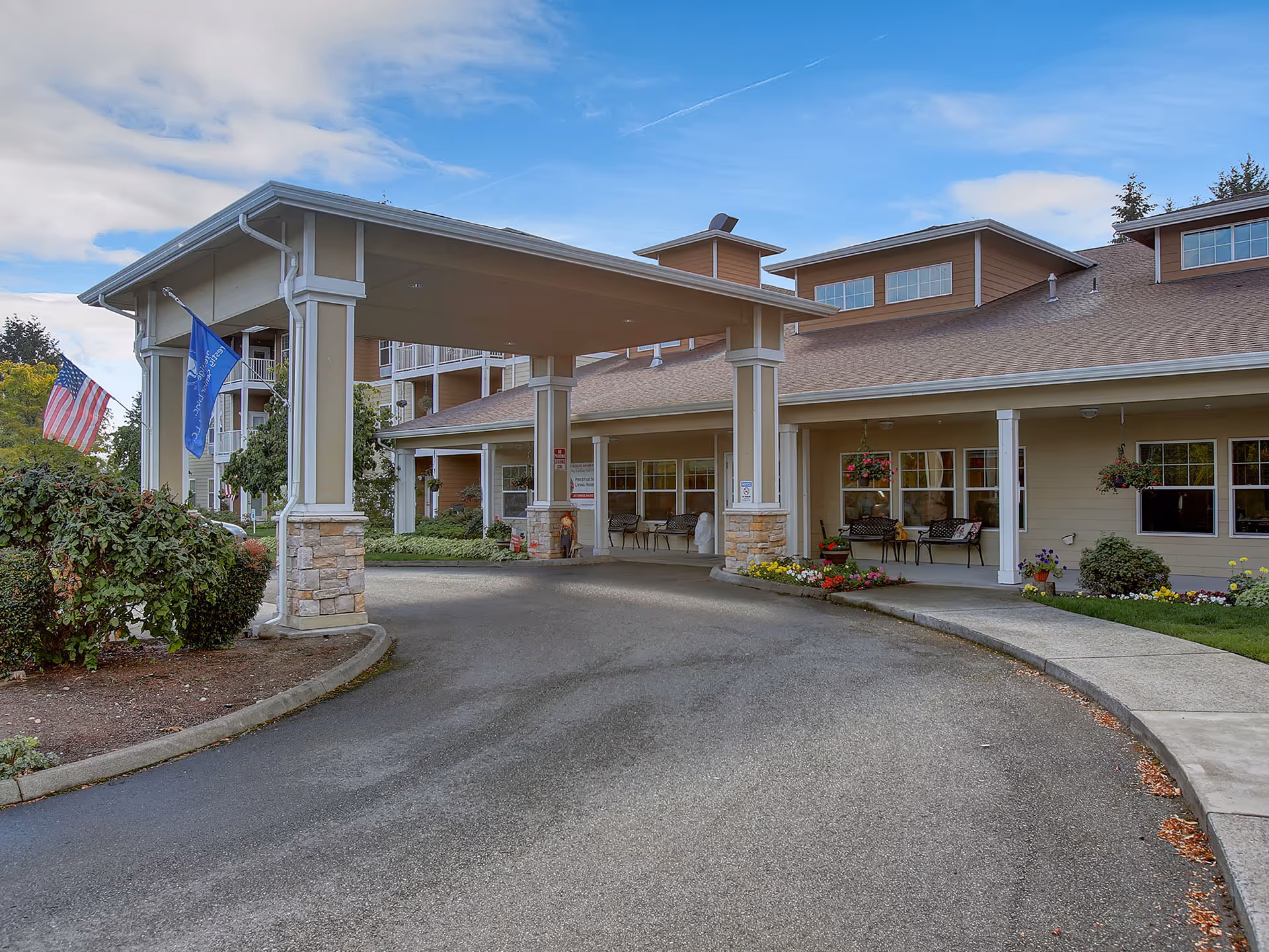 A senior living facility entrance with a covered porte-cochere and flags