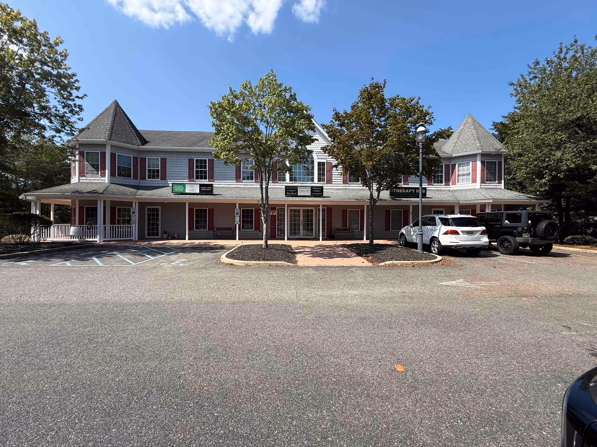 Two-story senior living facility with turreted corners, a front porch, and parked cars.