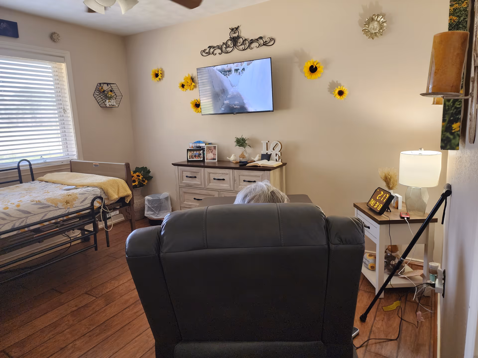 Cozy living area featuring a bed, couch, TV, and sunflower wall decor.