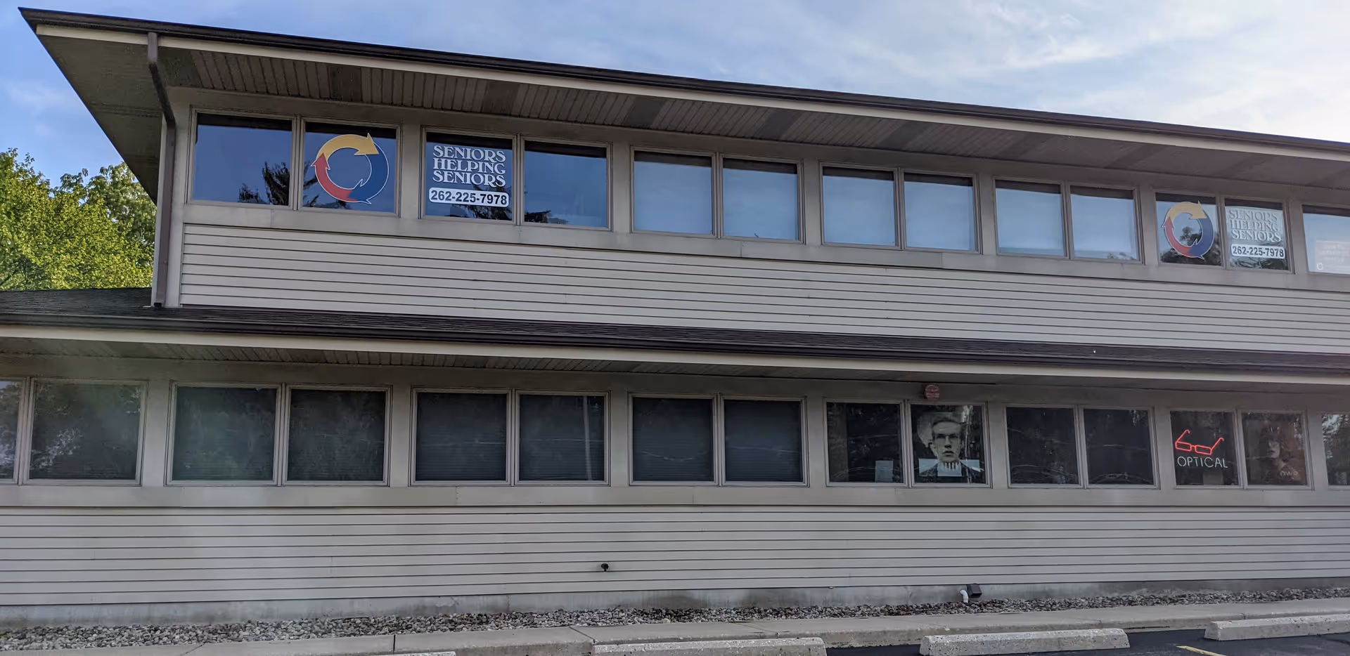 Two-story beige building exterior with window signs advertising Seniors Helping Seniors Waukesha County.
