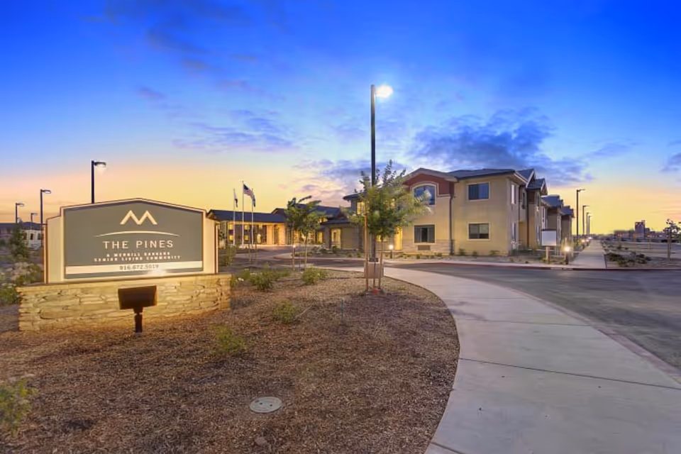 Exterior view of The Pines senior living community with a curved driveway and sign.