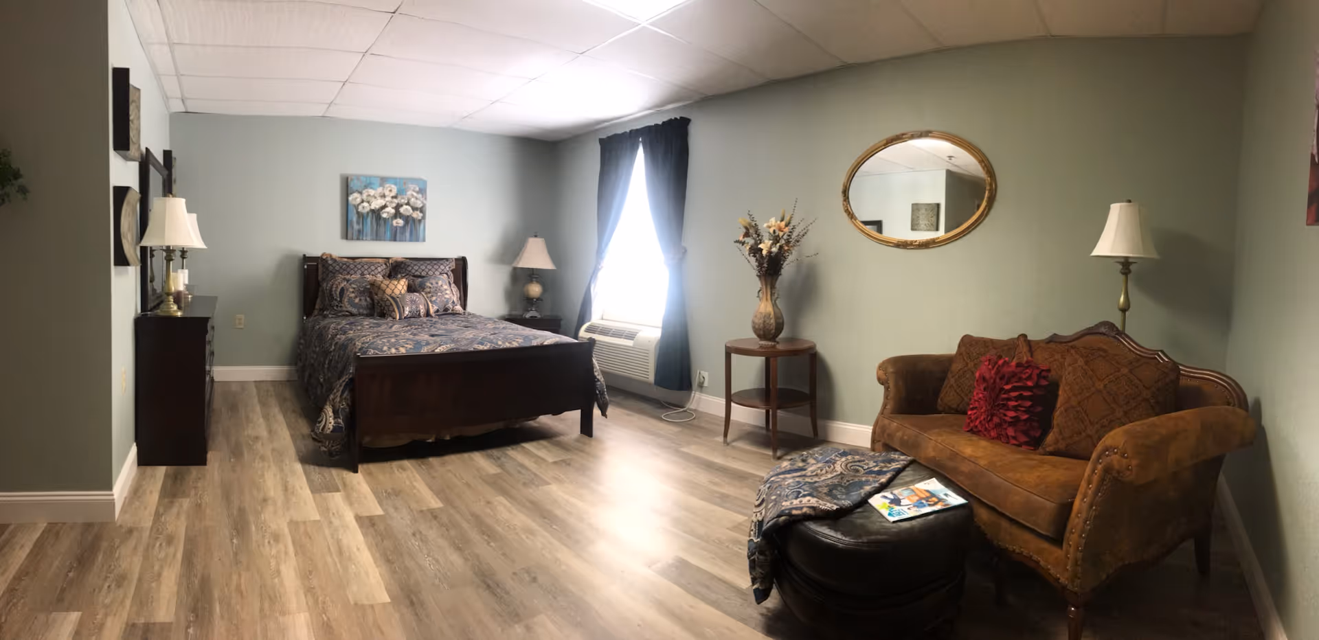 A spacious bedroom at Renaissance Home Northampton with a bed, sofa, lamps, and window.