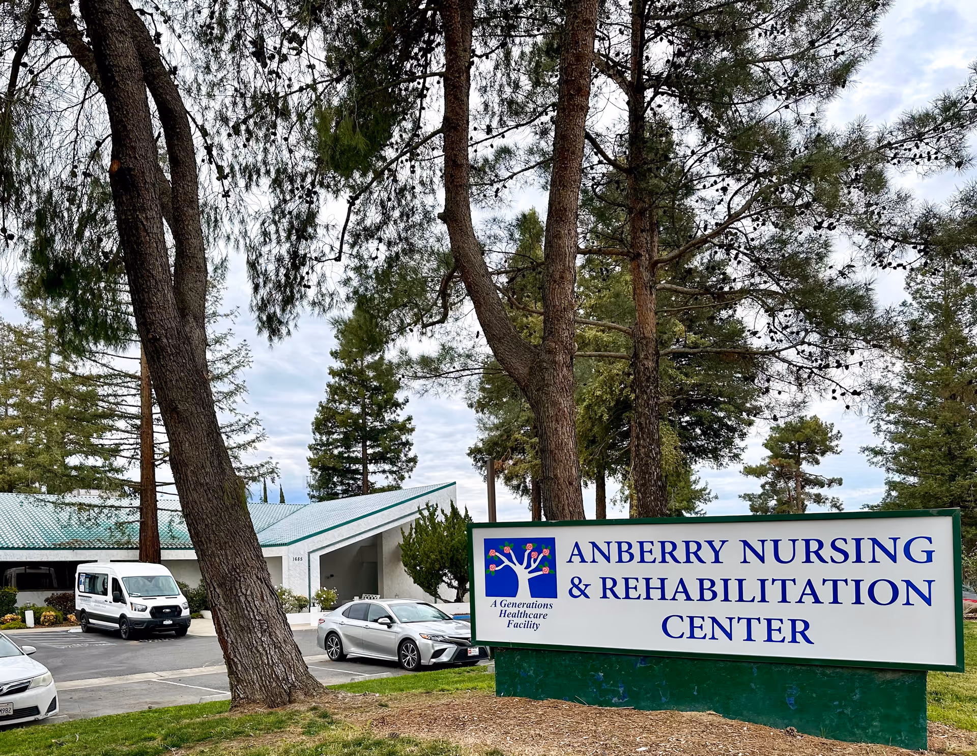 Exterior view of Anberry Nursing and Rehabilitation Center with a large sign and parked cars.