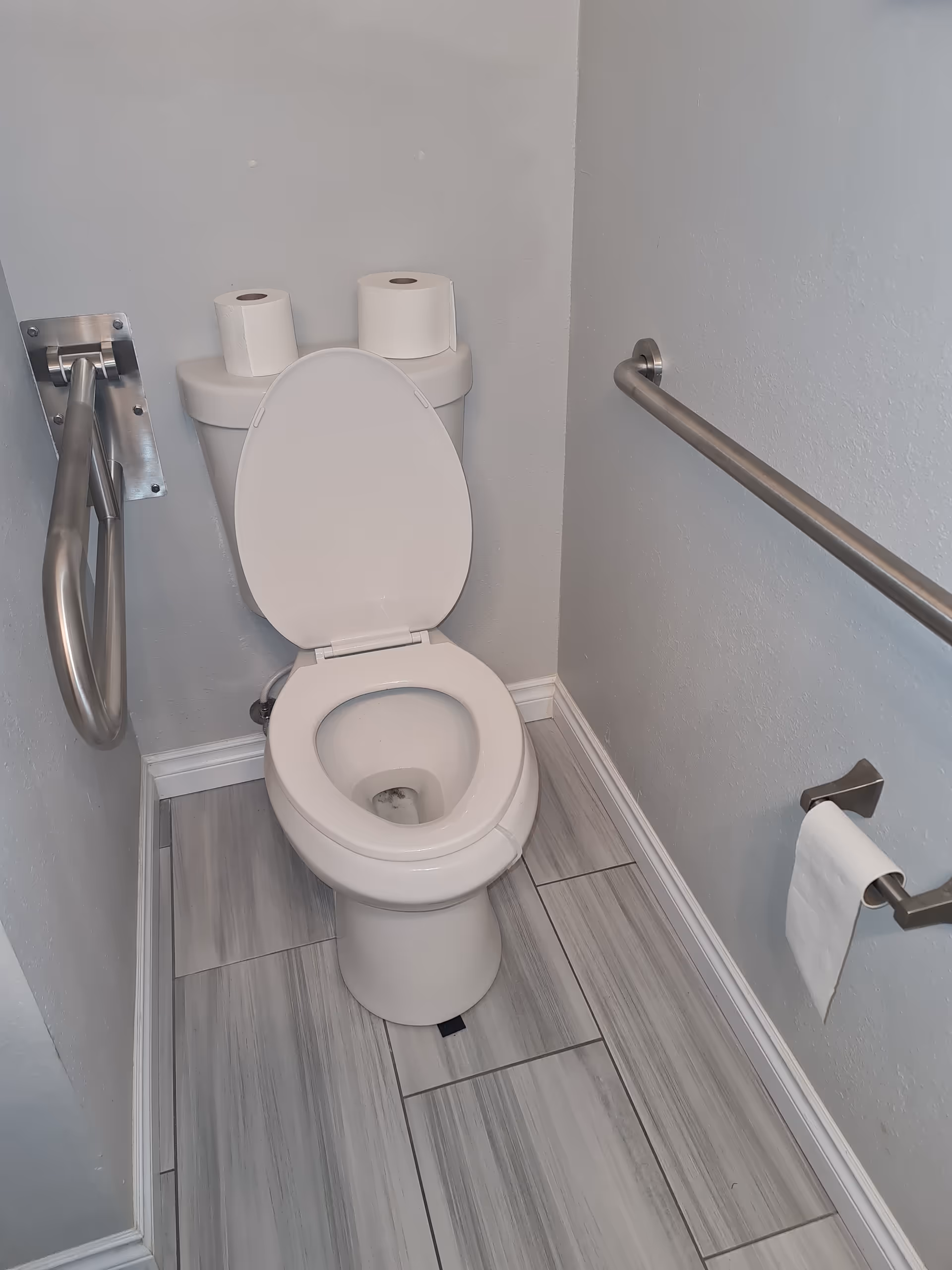 ADA-accessible bathroom with a toilet, metal grab bars, and two rolls of toilet paper.
