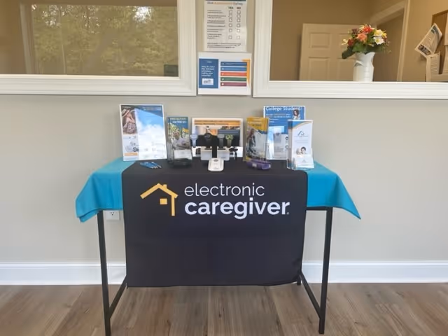 A brochure table with a blue cloth and electronic caregiver banner in a facility reception area.