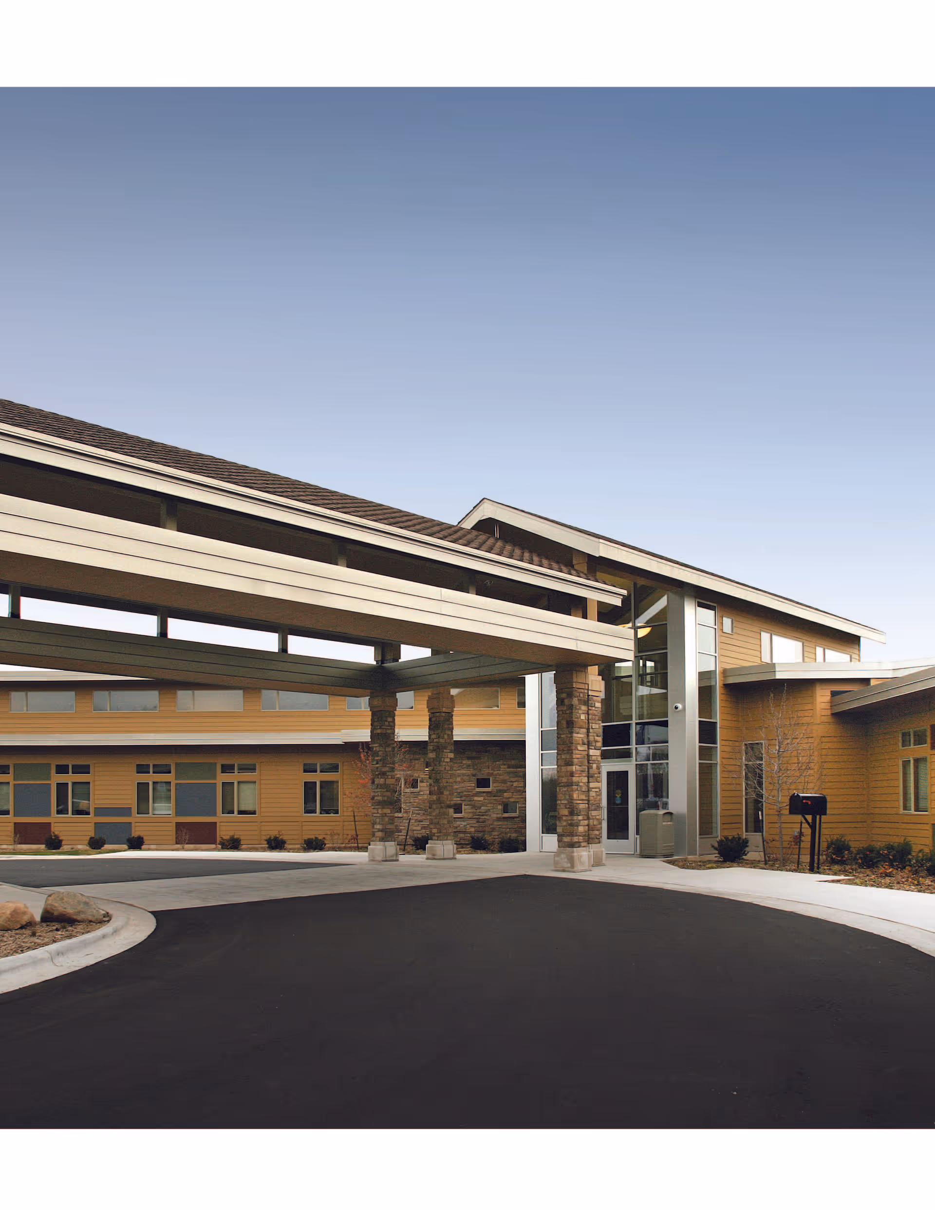 Modern senior living facility exterior with a covered entrance and curved driveway.