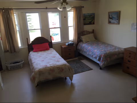 Two single beds with wooden headboards and nightstands by a windowed wall in a bedroom.