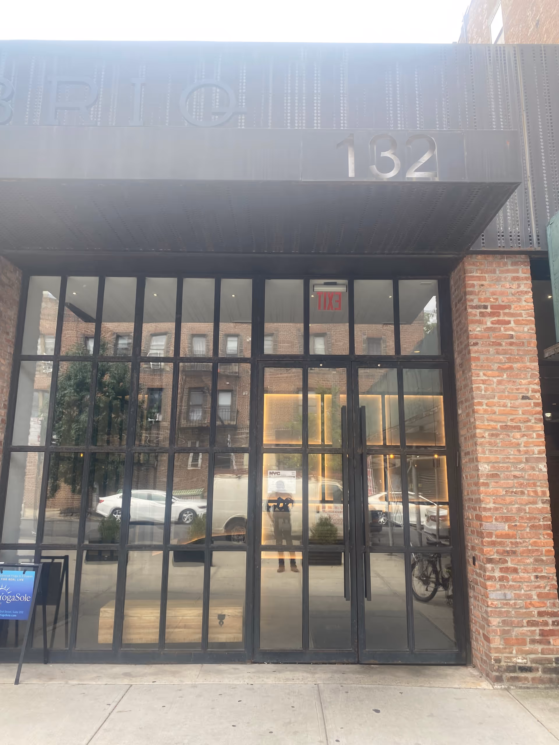 Modern glass entrance with metal frame and brick exterior, displaying 132.