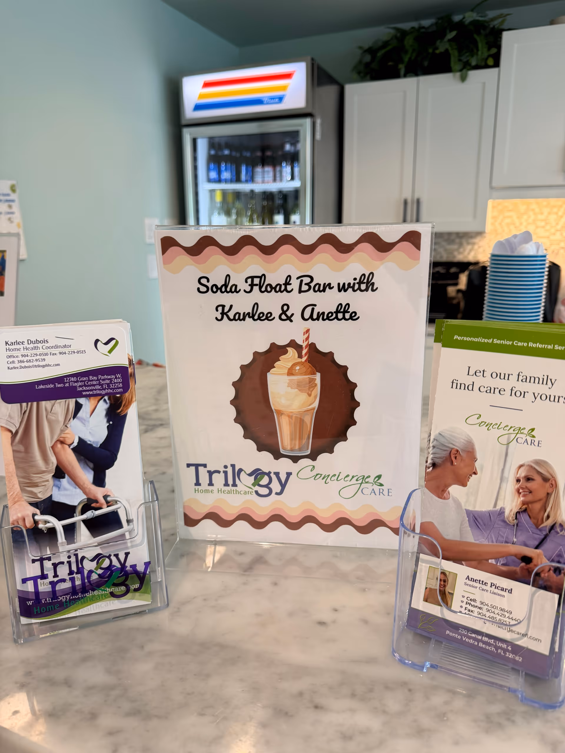 Indoor counter area with a soda float sign, brochures, and a beverage fridge.
