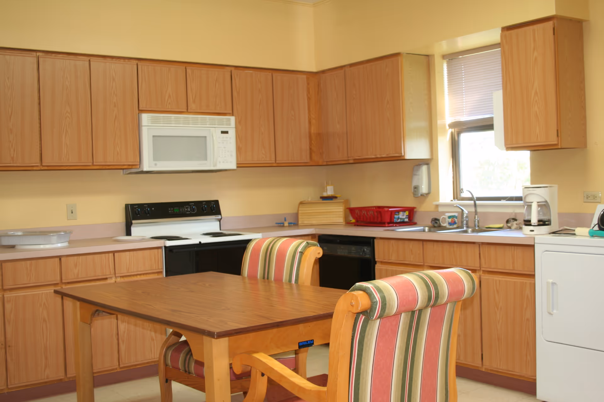 Kitchen area with wooden cabinets, a stove and microwave, sink and a table with striped upholstered chairs.