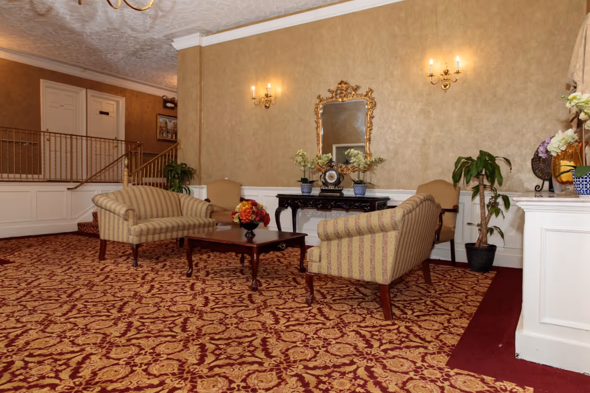 Lobby seating area with striped upholstered sofas, a coffee table, ornate mirror, plants and patterned carpet.