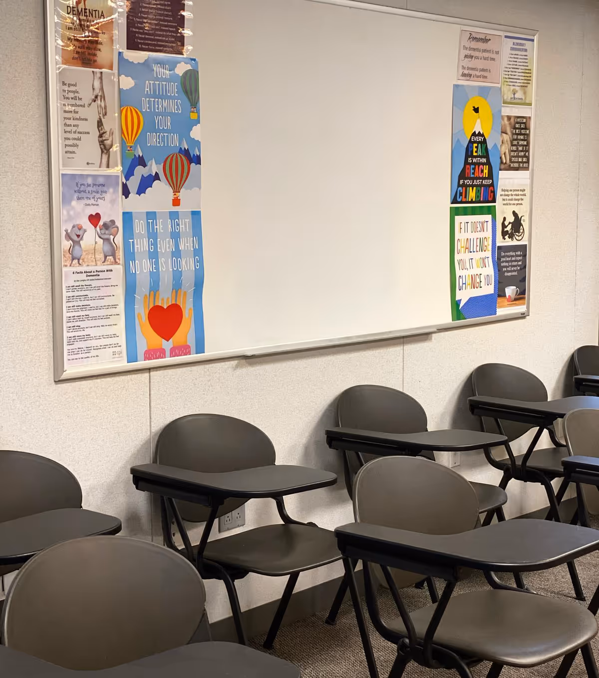 Rows of gray folding desks with attached chairs face a whiteboard in a classroom-style room.