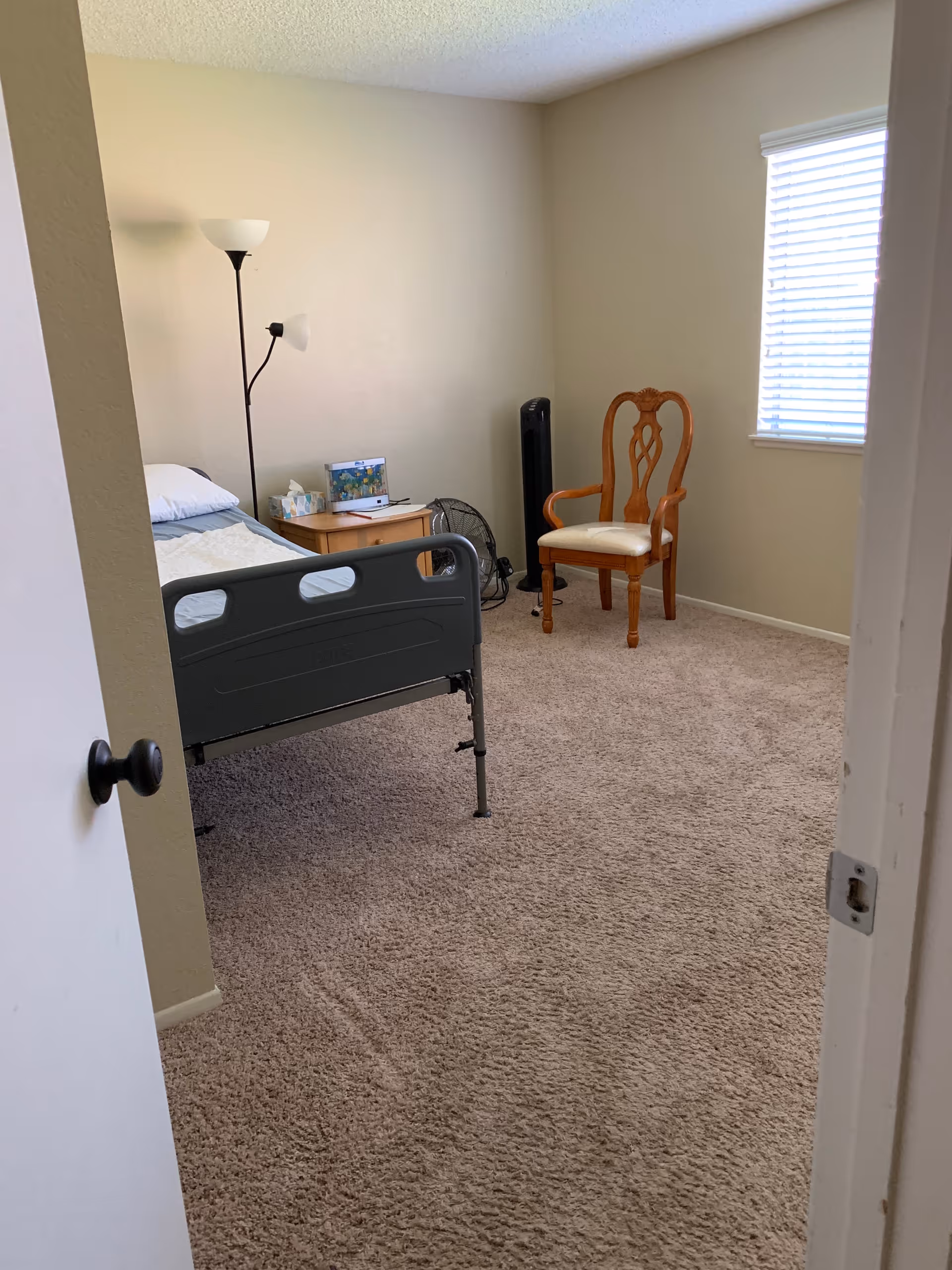 Bedroom with bed, nightstand, lamp, fan, wooden chair, and window.