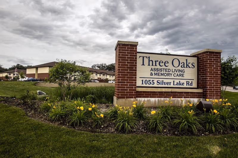 Brick sign for Three Oaks Assisted Living and Memory Care surrounded by yellow flowers.