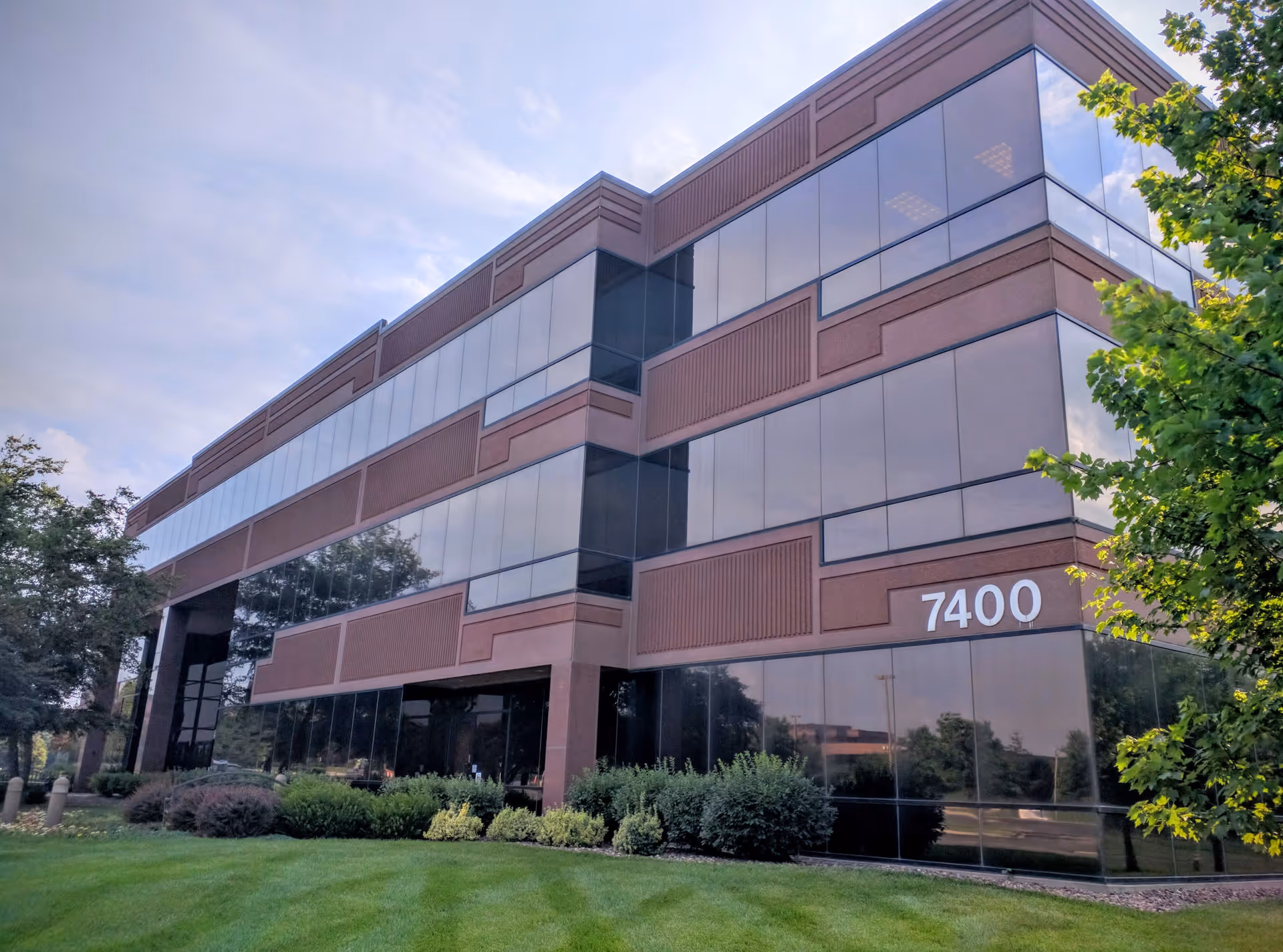 Modern glass-brick office building with manicured lawn and the number 7400 on the facade.