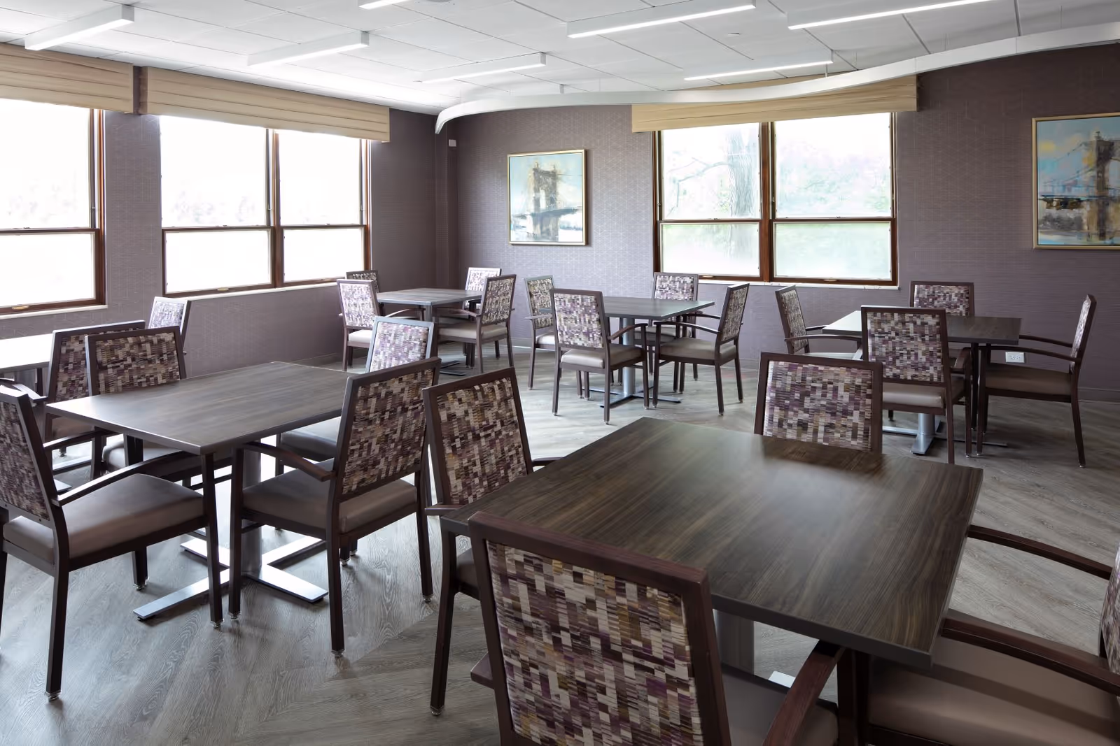 Dining room in a senior living facility with dark wood tables and patterned chairs.
