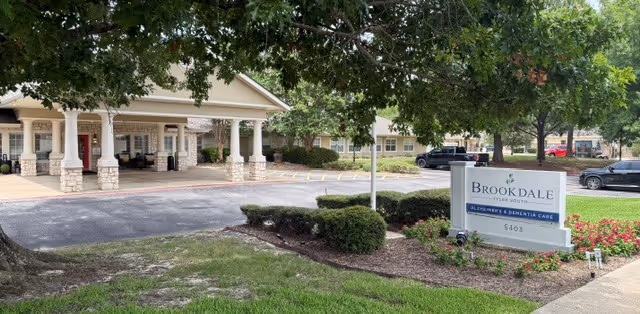 Exterior view of a senior living facility with a covered entrance and landscaped front yard.