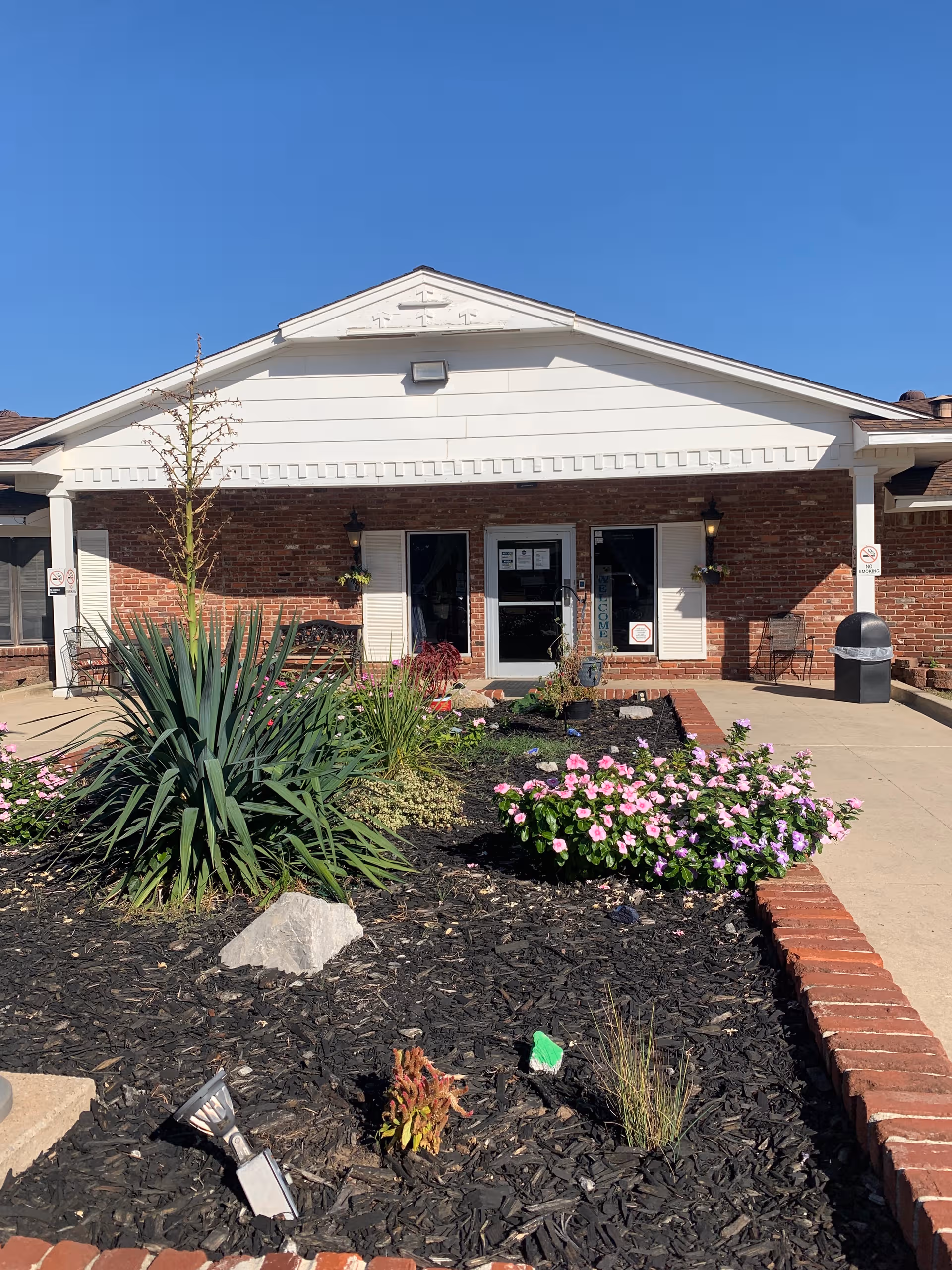 Exterior of Windsor Hills Nursing Center with brick facade, doors, and landscaped garden.
