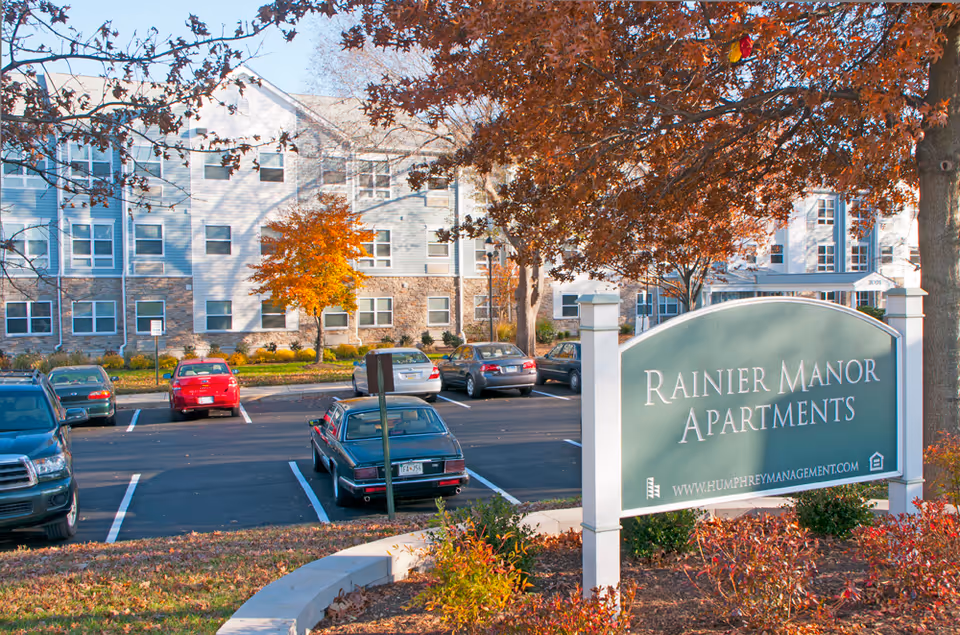Autumn scene at Rainier Manor Apartments featuring parking lot, sign, and multi-story building.