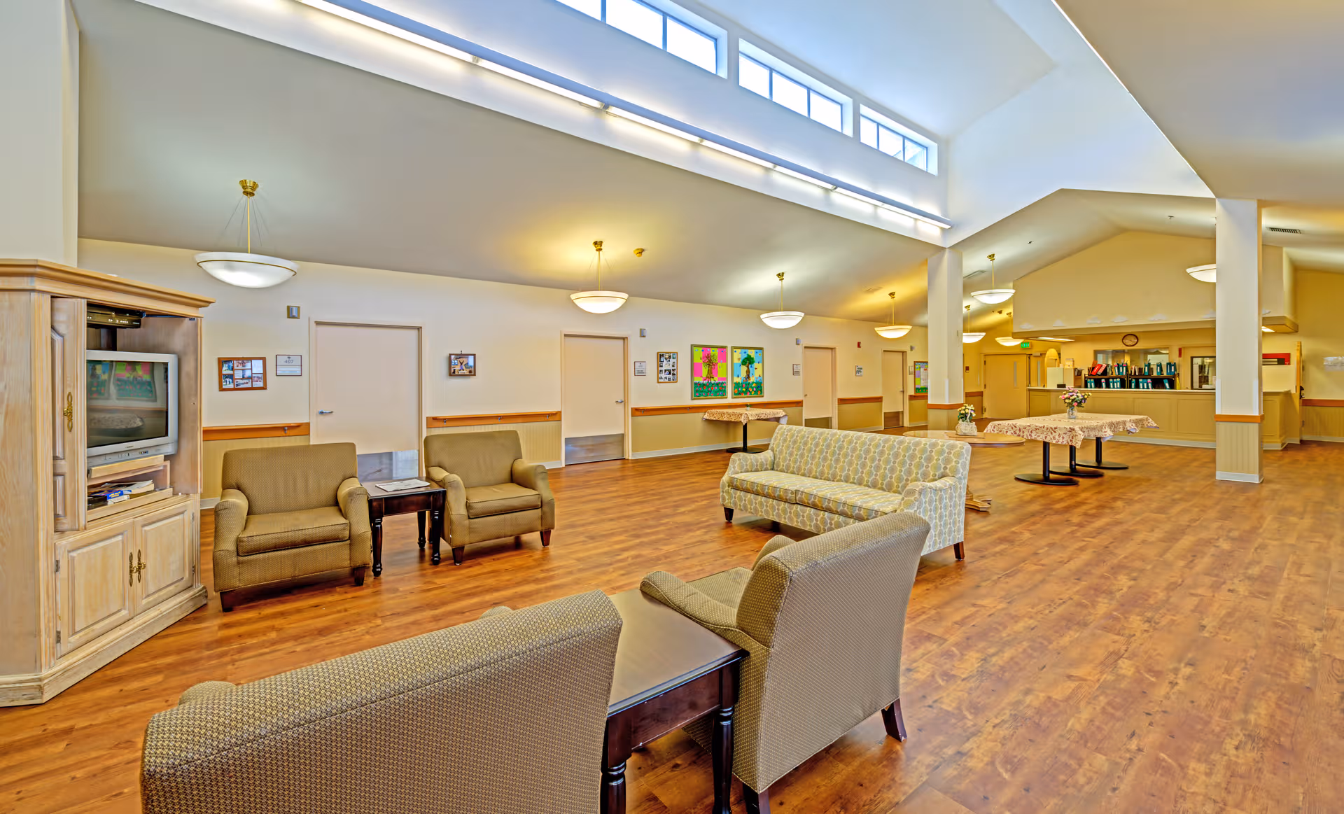 Spacious senior living lounge with sofas, chairs, tables, and a back-counter area.