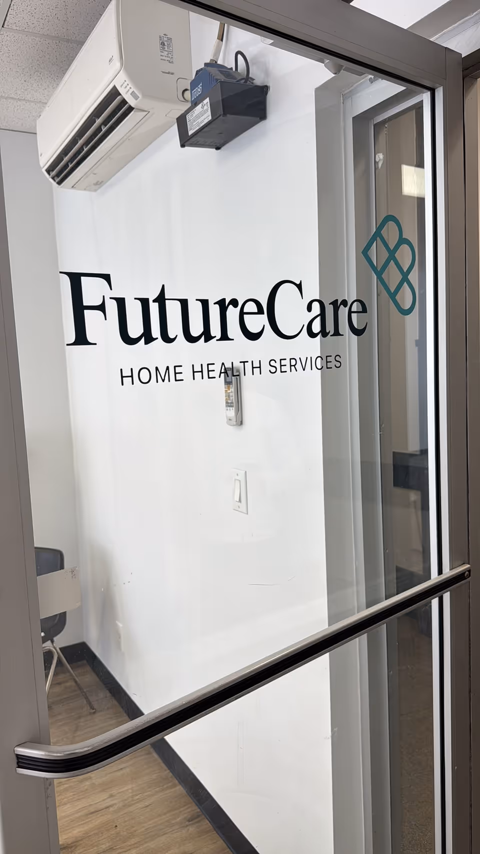 Interior view of FutureCare Home Health Services logo on a white wall beside glass doors.