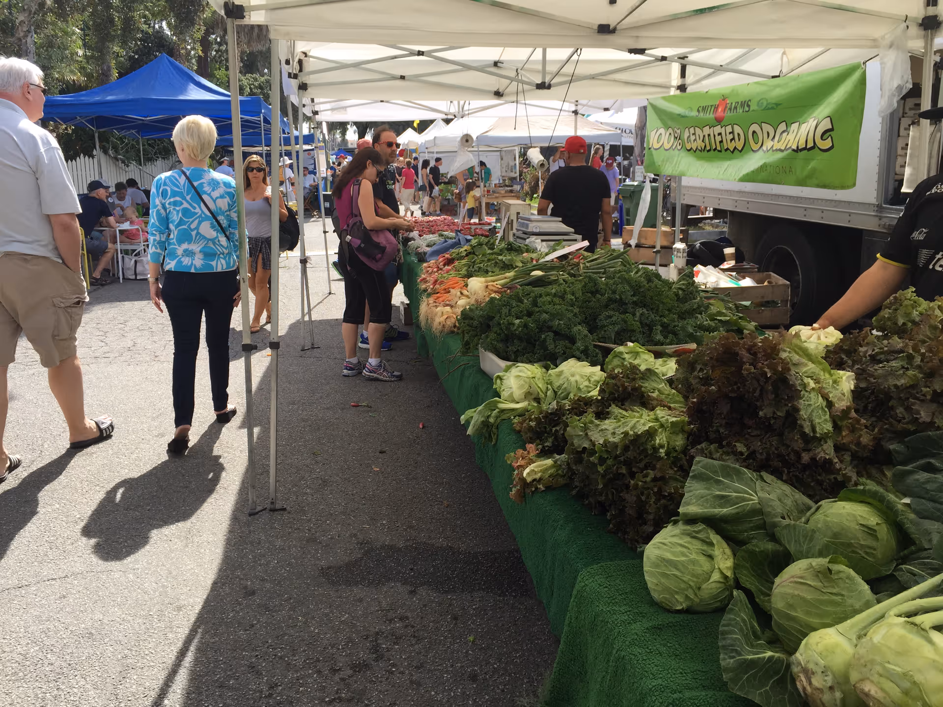 Outdoor market stalls under tents with fresh produce and shoppers walking along a street