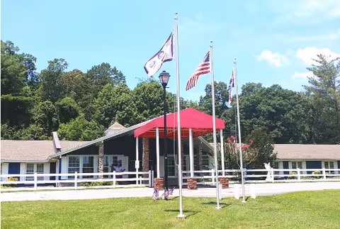 Front exterior of Wilham Ridge Assisted Living with a red canopy, flagpoles, and white fence.