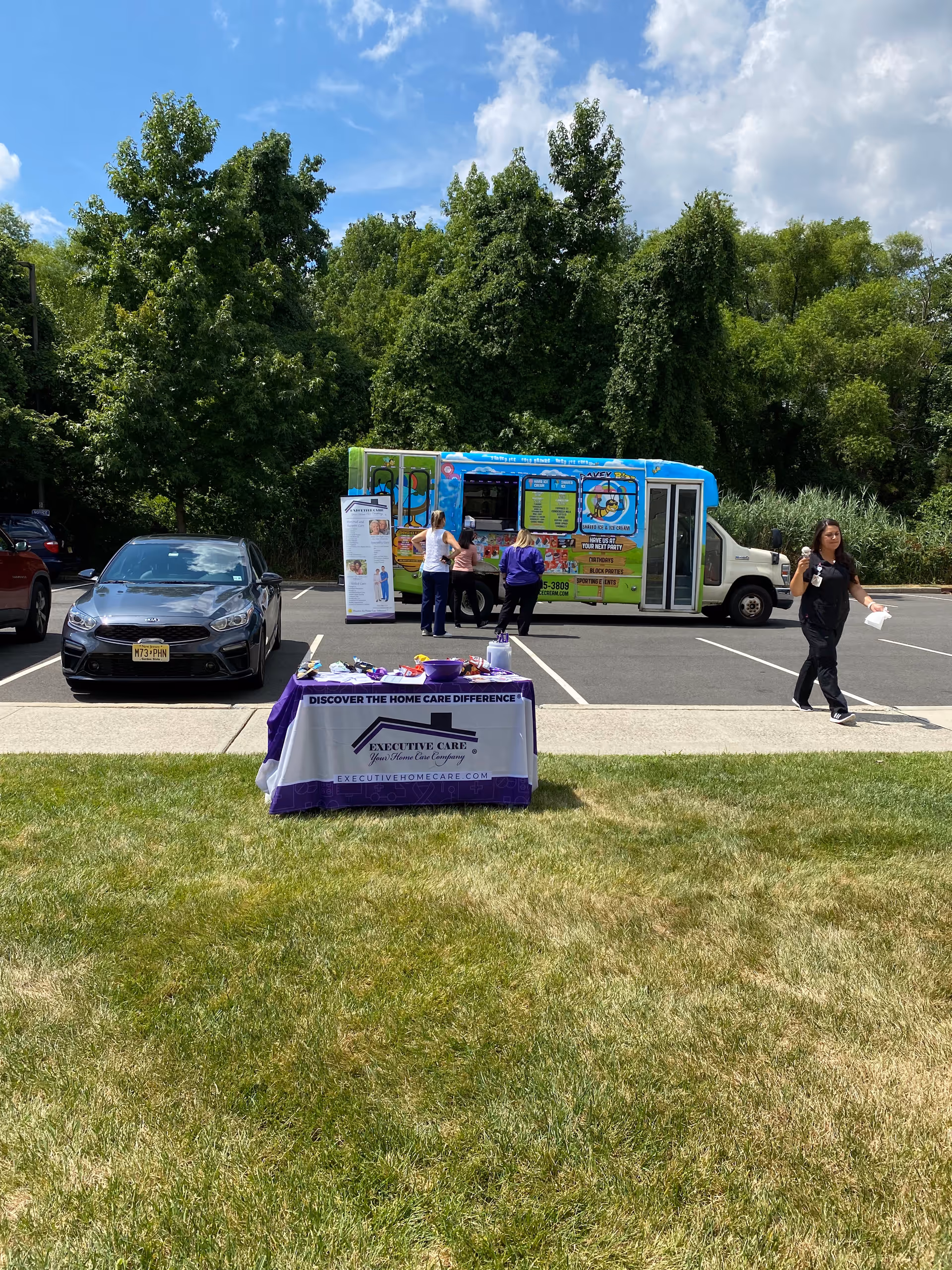 Outdoor promotional event with a purple table cover, a colorful van, and several people nearby.