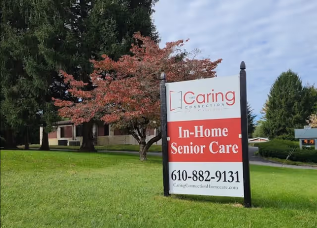 Lawn sign for The Caring Connection's In-Home Senior Care beside a building.