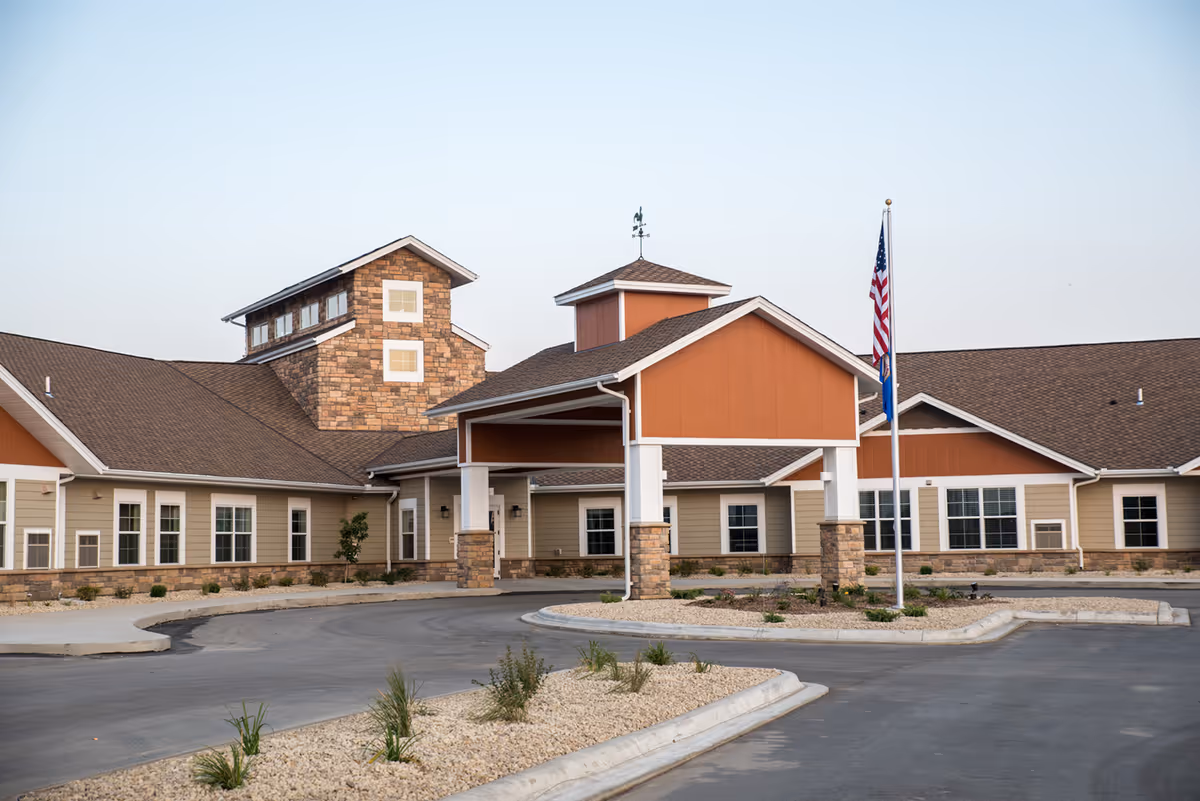 Exterior view of Meadow Place Assisted Living, showing entrance canopy and American flag at the front.