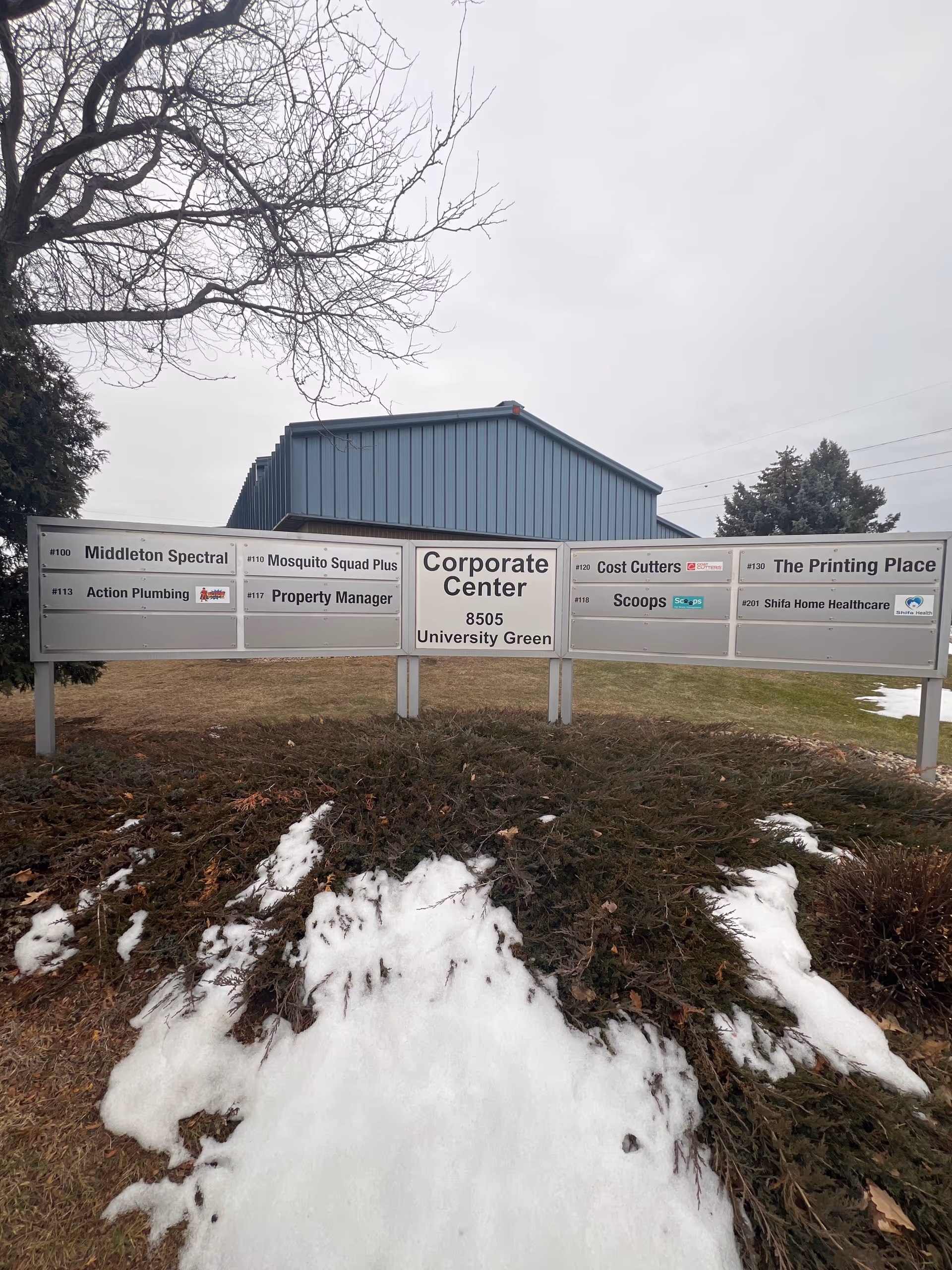 Exterior view of corporate center sign listing tenants, including Shifa Home Healthcare, with snow on ground.