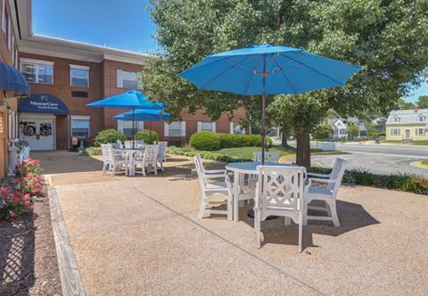 Outdoor seating patio at Healing Rivers with blue umbrellas and white tables beside the brick building.
