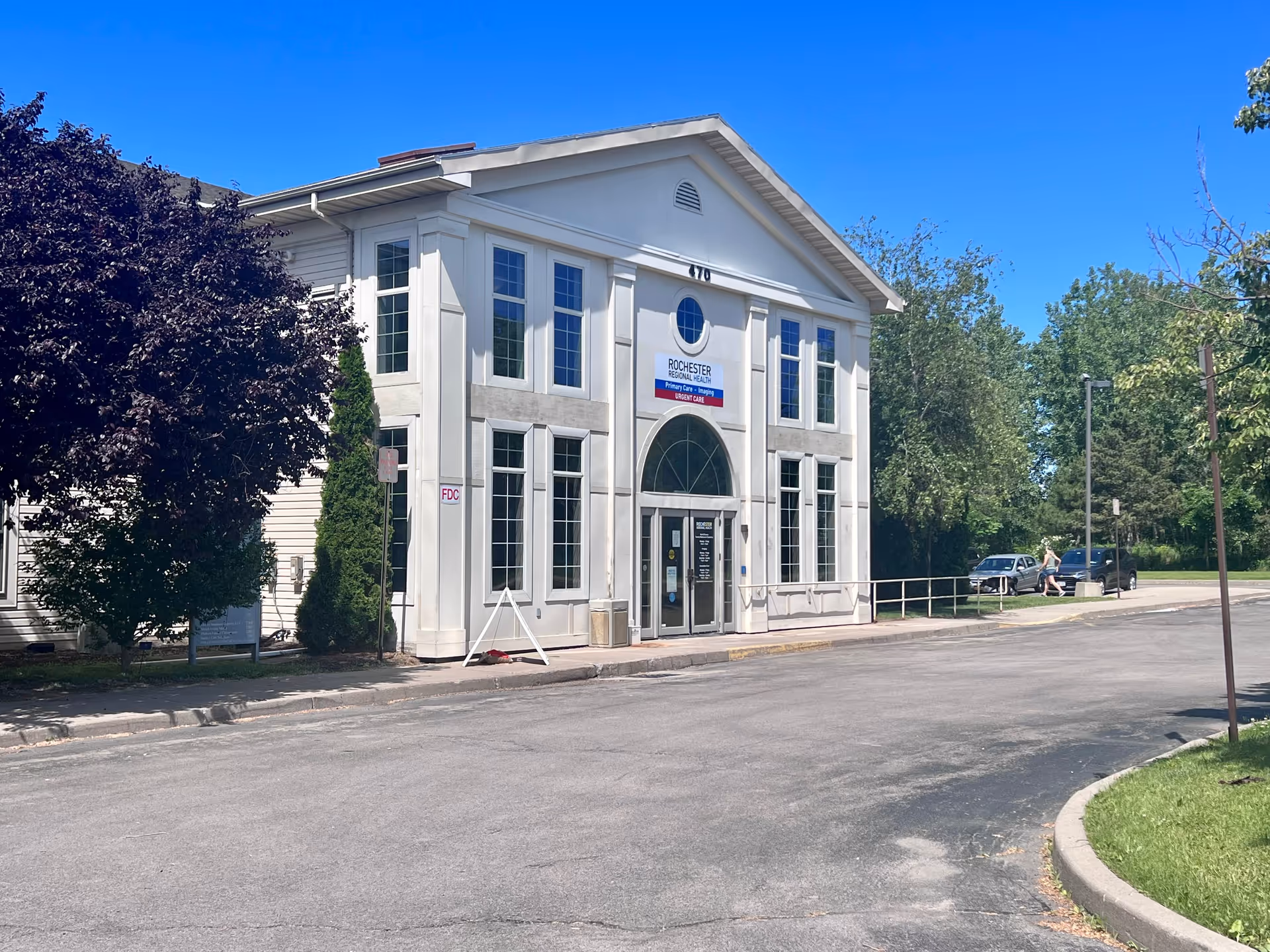 White two-story building with arched entrance and large windows on a sunny day