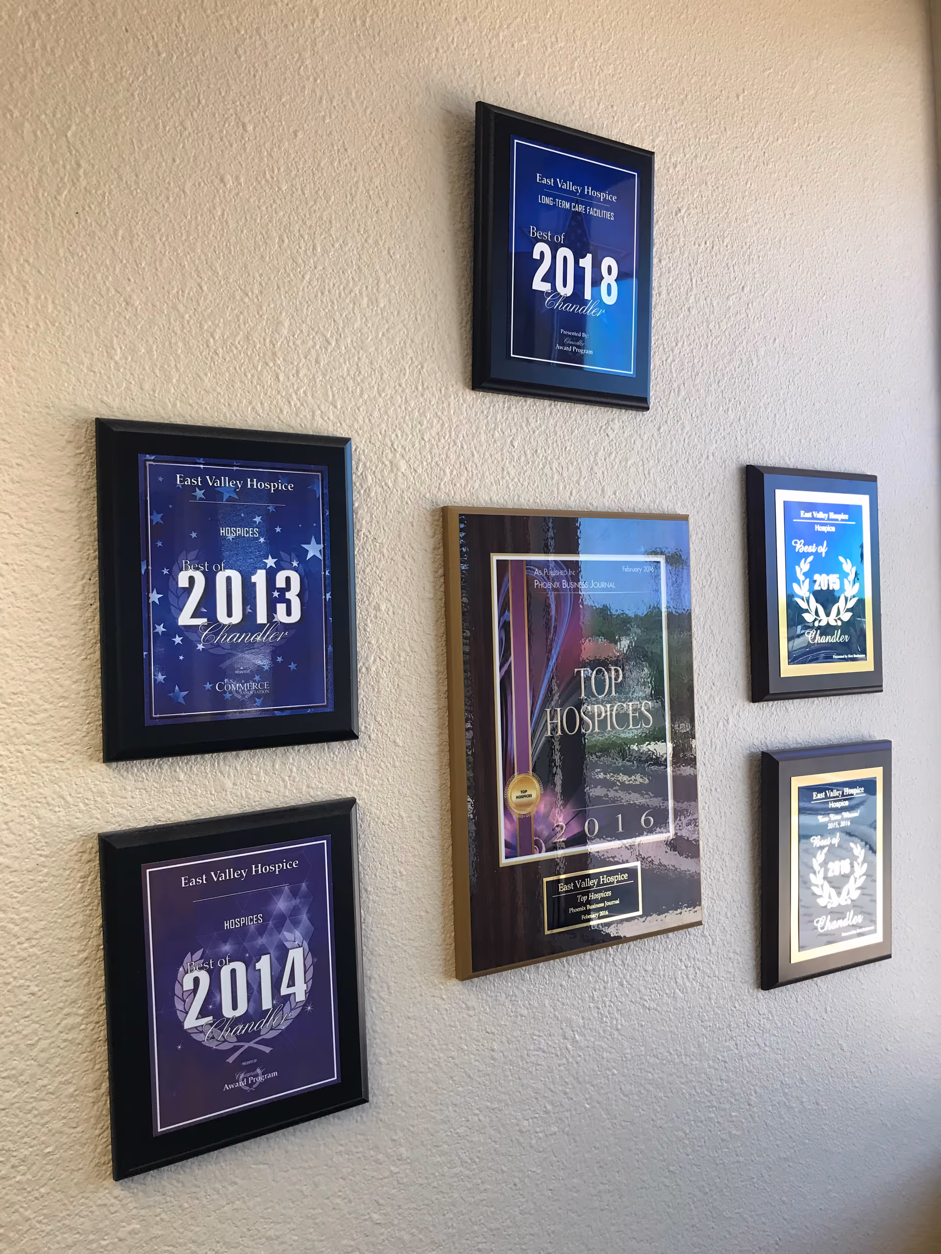 Wall mounted with framed awards for Casa de la Luz East Valley Hospice inside a hallway.
