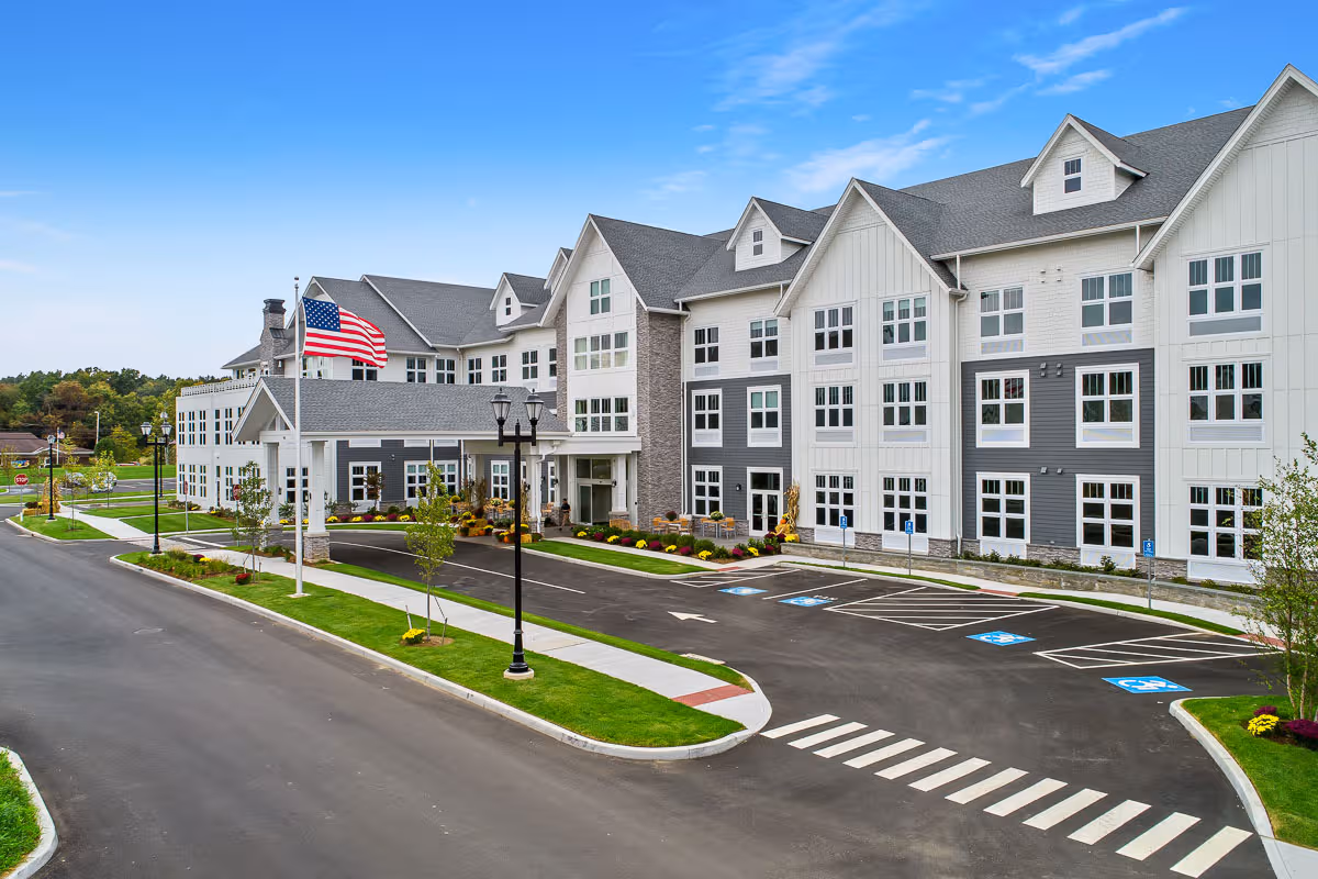 Wide exterior view of Skybrooke at Simsbury, a multi-story senior living building with parking and landscaping.