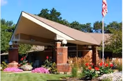 Front exterior of Rose Garden senior living facility with flag and flowers.