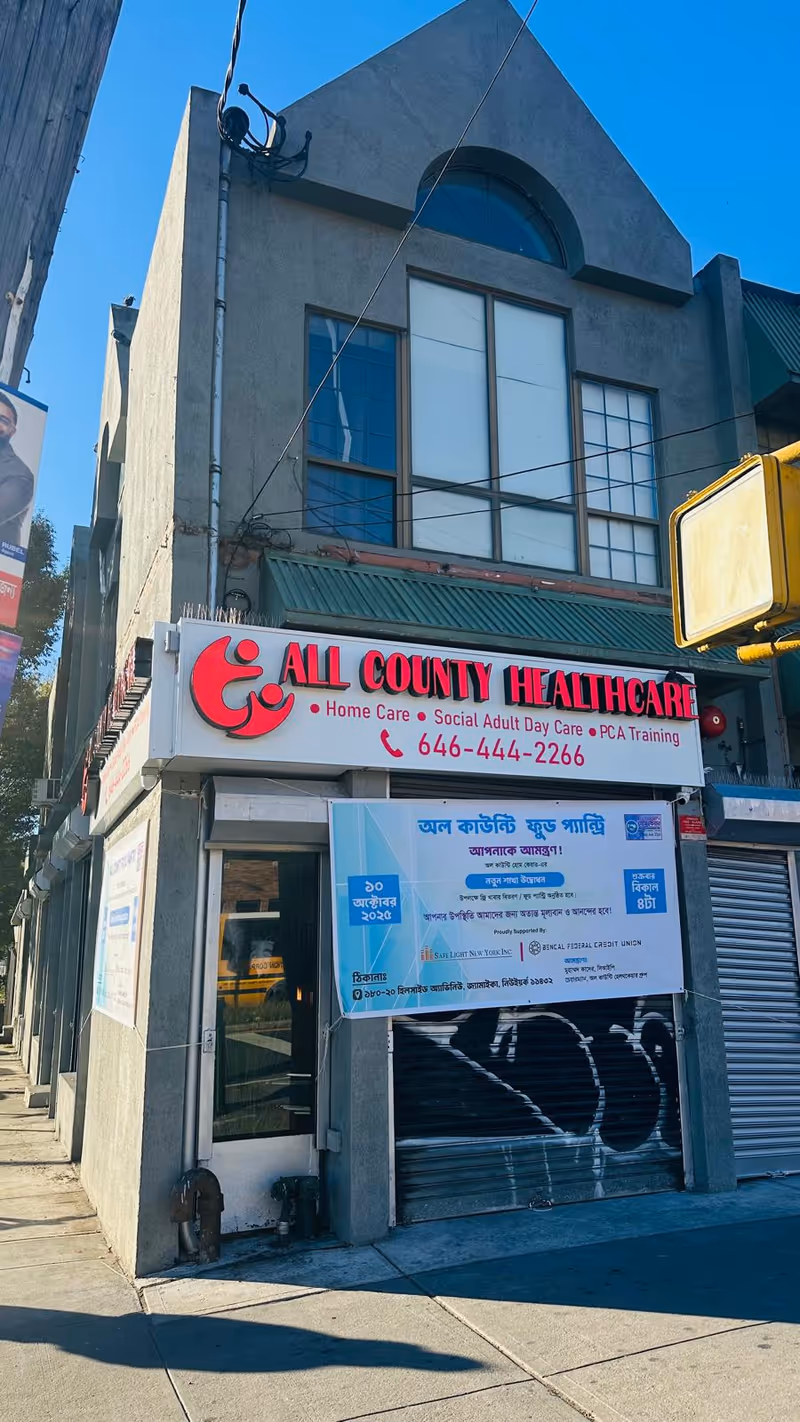 Two-story grey building with a red All County Healthcare sign on storefront and banner.