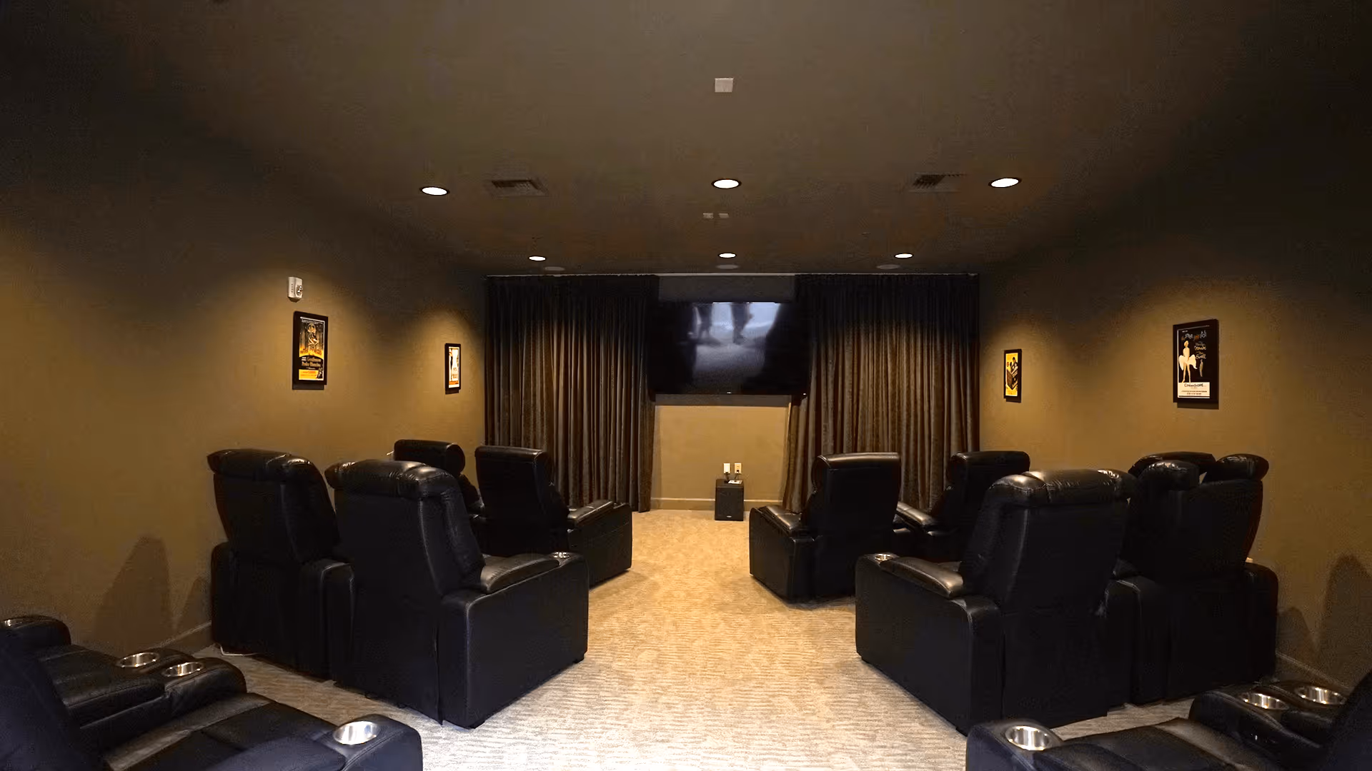 Small theater-style room with black leather recliners arranged facing a wall-mounted TV and dark curtains.