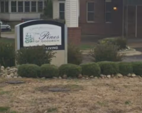 Exterior view of a senior living facility entrance with a sign and trimmed bushes