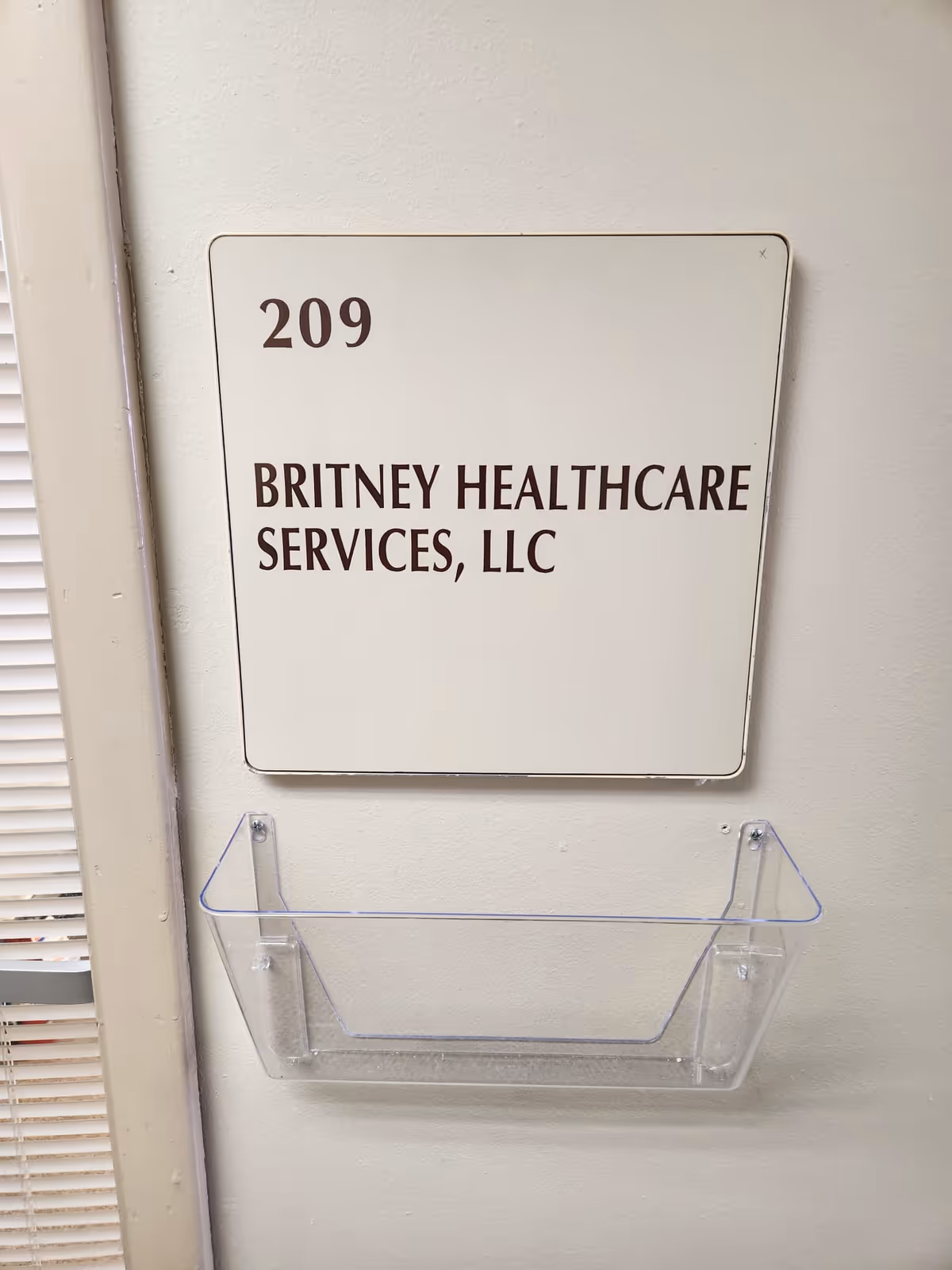 Wall plaque shows 209 Britney Healthcare Services, LLC, with a clear wall-mounted shelf.