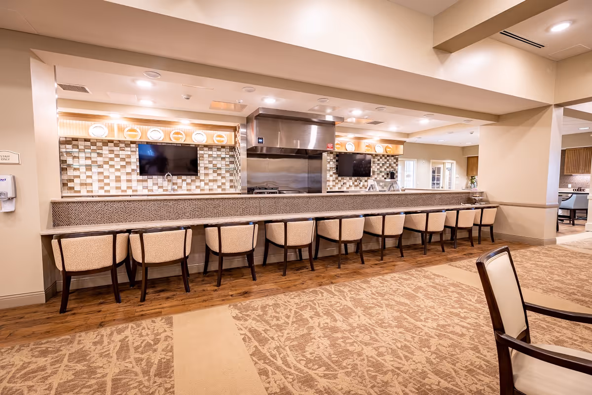 Long dining counter with beige chairs and a tiled backsplash in a senior living dining area.