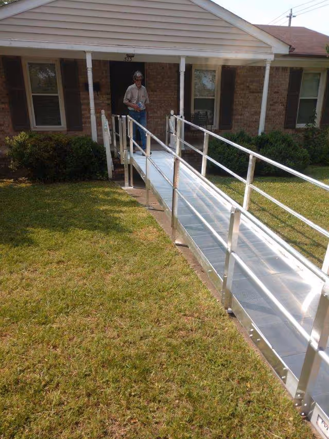 A metal wheelchair ramp to a brick house front, with a person near the door.