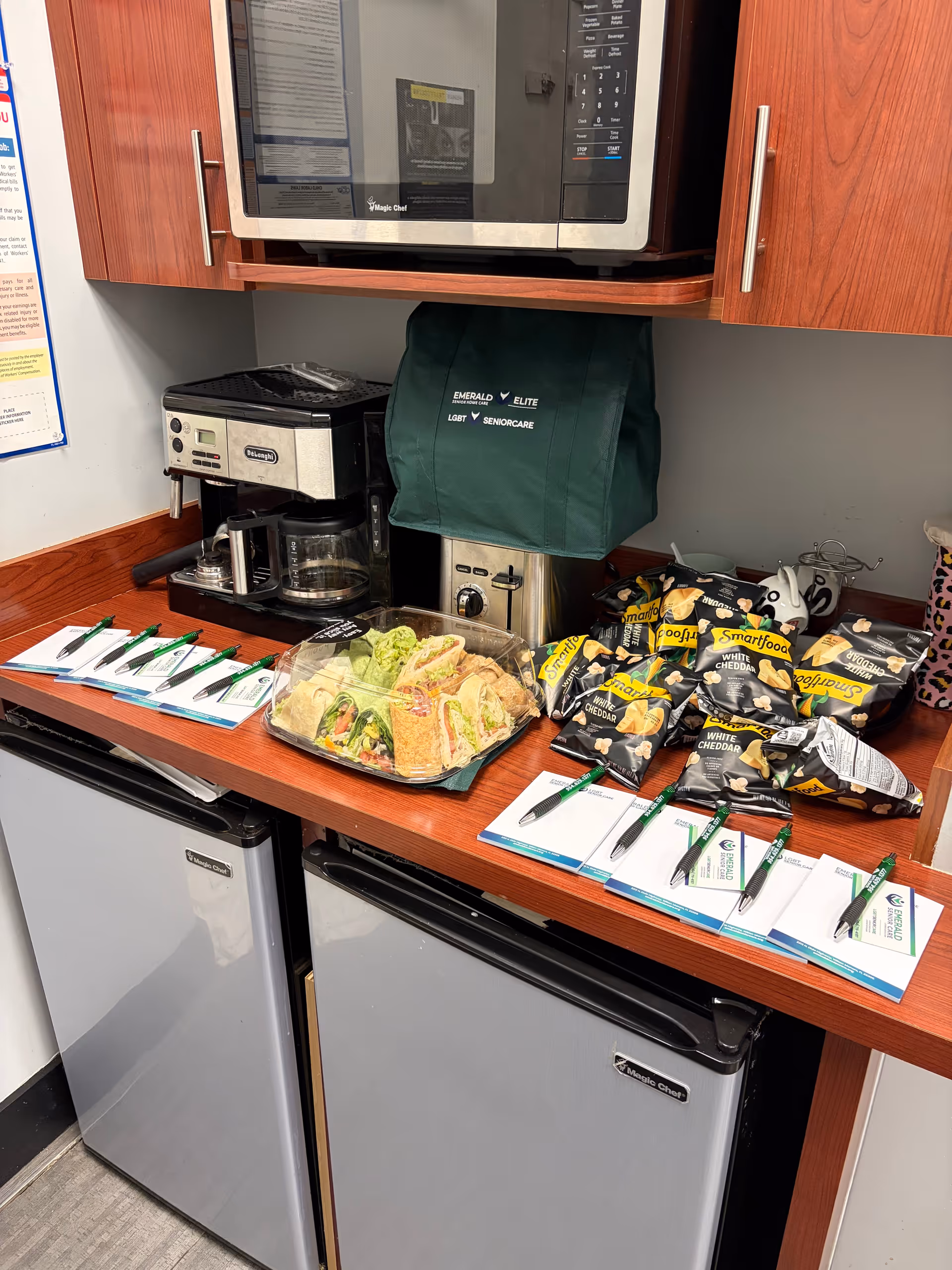 Kitchen counter with microwave, coffee maker, sandwiches, chips, and two mini-fridges.