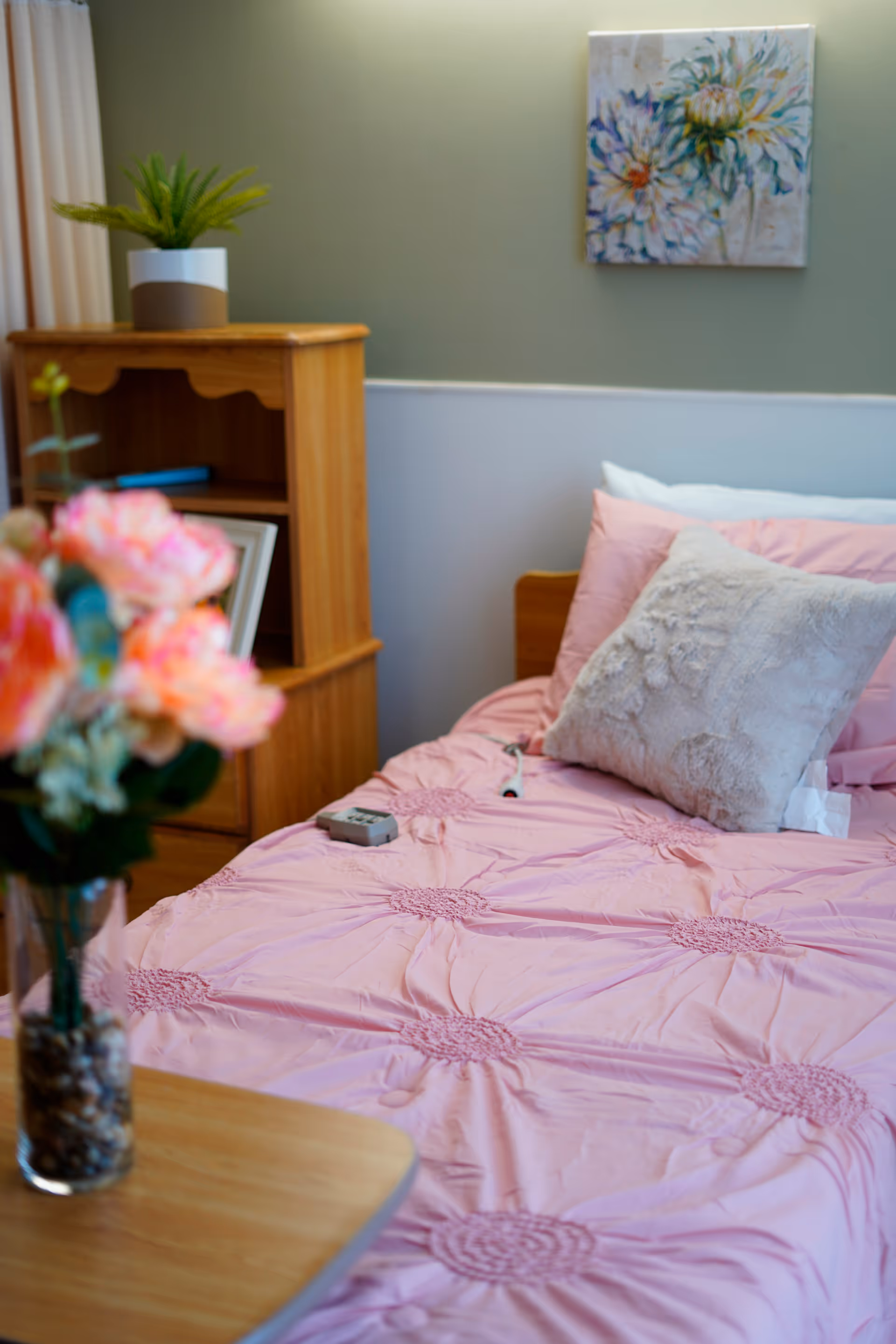A pink bed with pillows and wooden furniture in a cozy senior living bedroom.