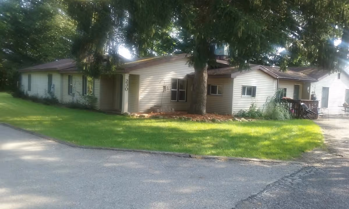 Single-story white building with a green lawn and trees along a street.