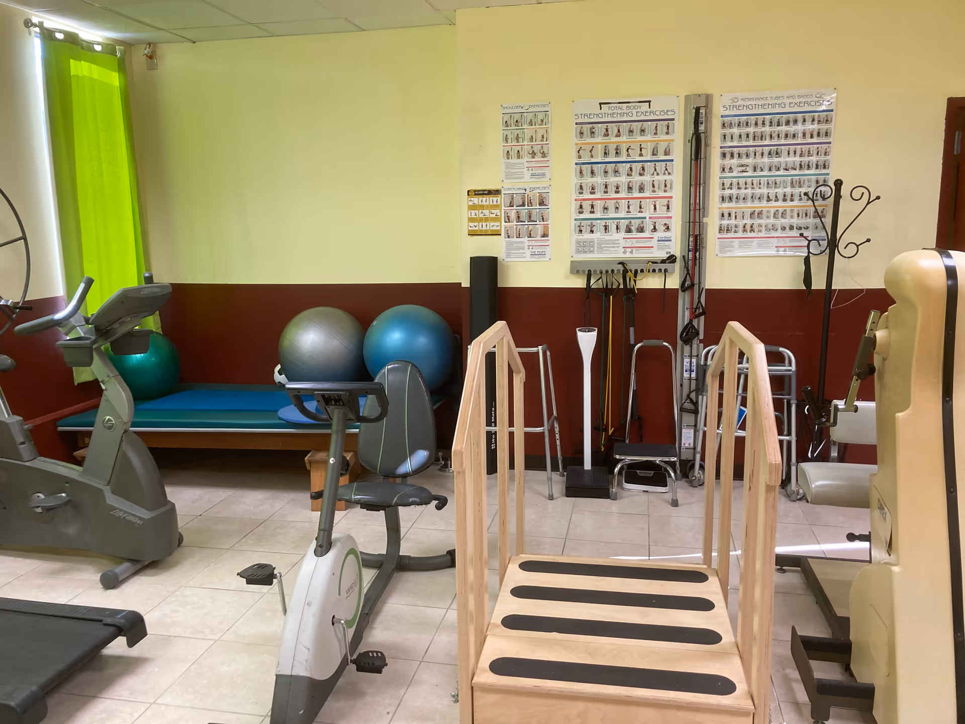 Indoor physical therapy room with exercise equipment, balance bars, and posters.