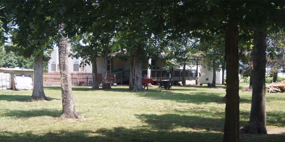 Exterior view of a senior living facility with a shaded outdoor seating area and trees.