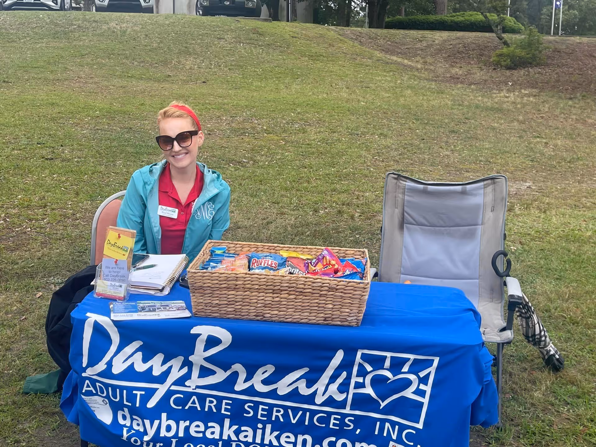 Staff member sits at a DayBreak table outdoors with snacks on a grassy hill.