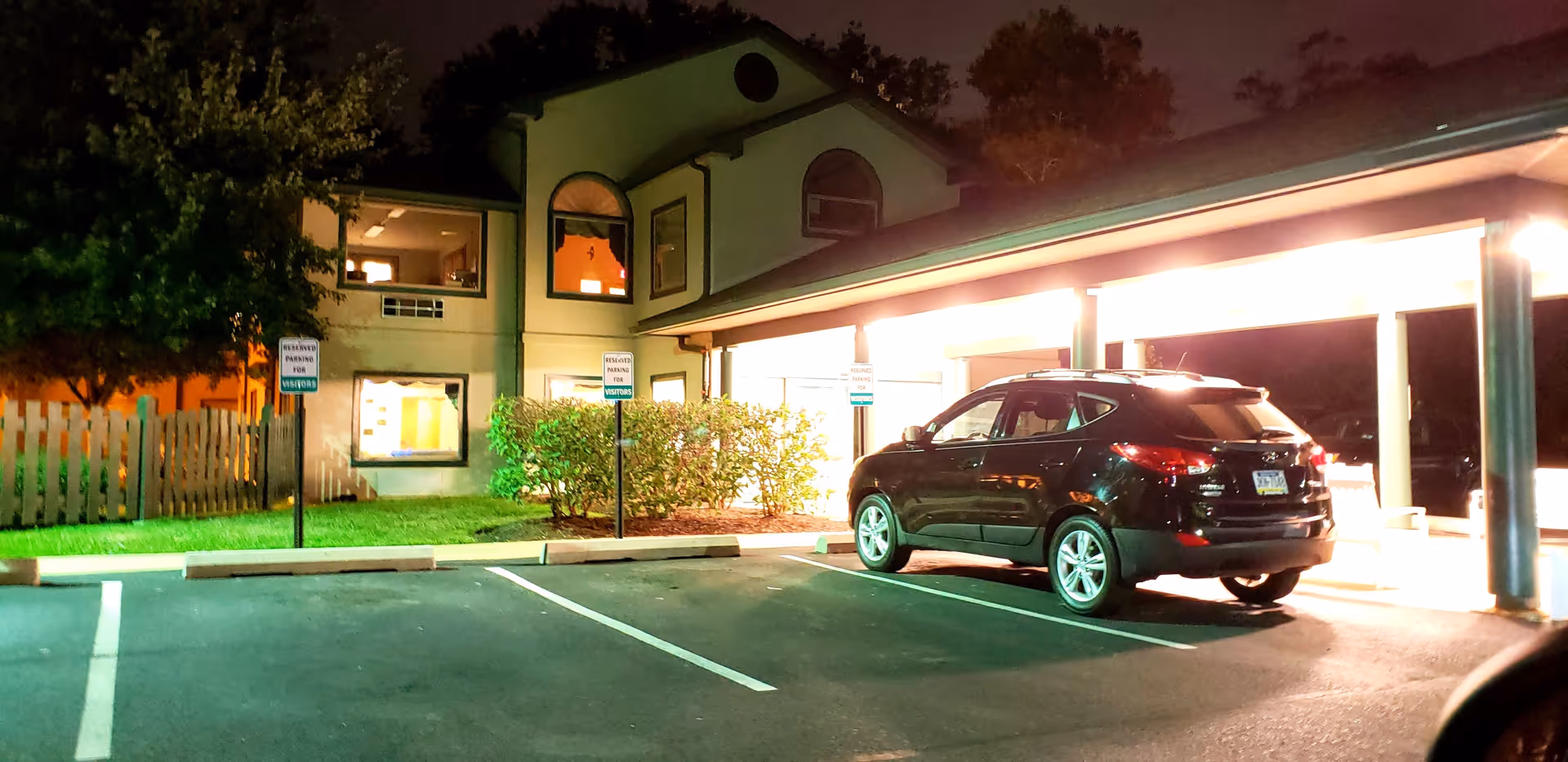 Night exterior view of Naamans Creek Country Manor with a parked SUV near a covered entrance.